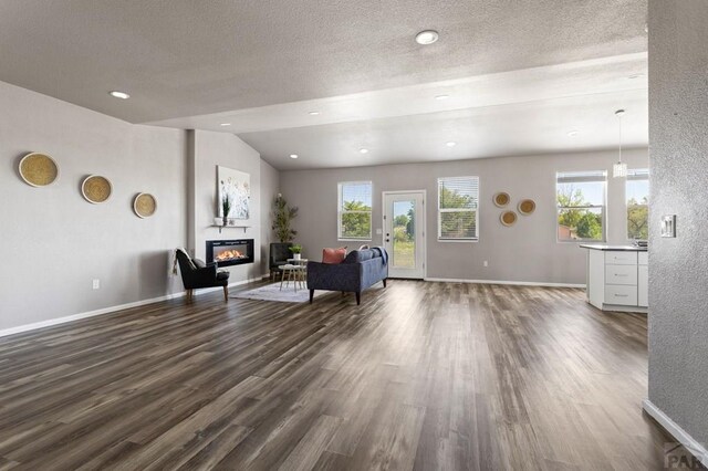 living area featuring baseboards, dark wood-style flooring, a glass covered fireplace, and a healthy amount of sunlight