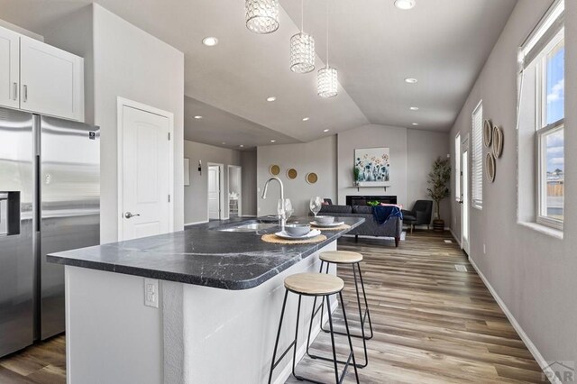 kitchen with stainless steel fridge, white cabinets, a kitchen breakfast bar, hanging light fixtures, and a sink