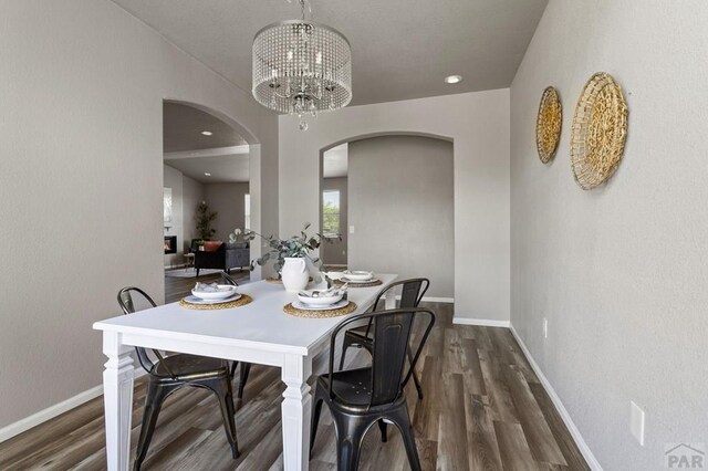 dining room with a chandelier, dark wood-style flooring, arched walkways, and baseboards