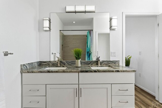 full bathroom with double vanity, wood finished floors, a sink, and a shower with curtain