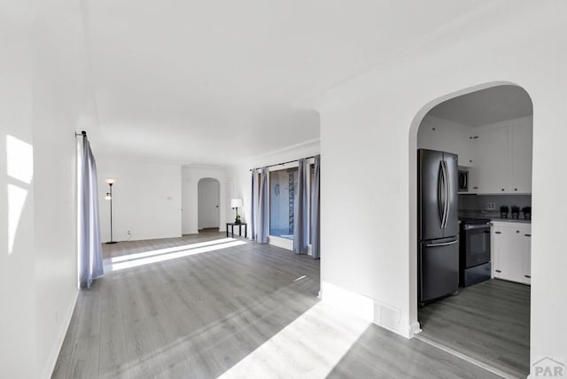 interior space with arched walkways, light wood finished floors, appliances with stainless steel finishes, open floor plan, and white cabinets