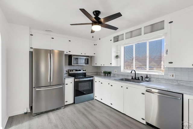 kitchen featuring light wood finished floors, appliances with stainless steel finishes, light countertops, white cabinetry, and a sink