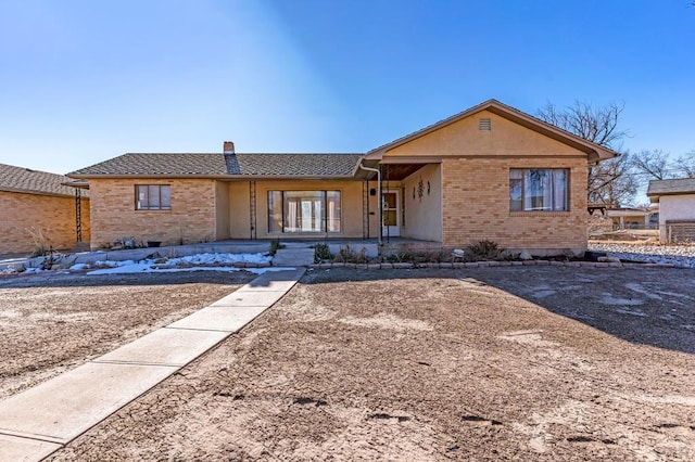 ranch-style house with covered porch, brick siding, a chimney, and stucco siding