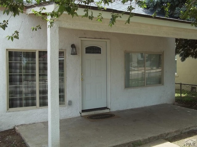 view of exterior entry with fence, a patio, and stucco siding