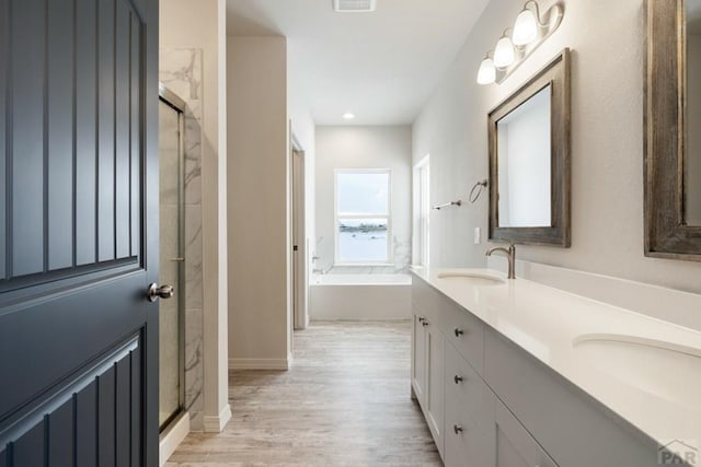 full bath featuring wood finished floors, a stall shower, a sink, and a bath