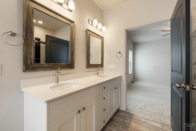 full bath with double vanity, wood finished floors, a sink, and baseboards