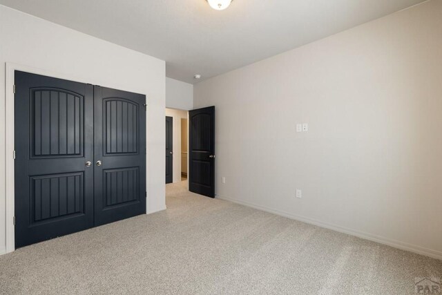 unfurnished bedroom featuring light carpet, baseboards, and a closet