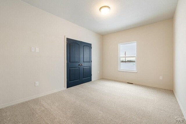 unfurnished room with carpet floors, visible vents, and baseboards