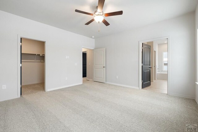 unfurnished bedroom with light carpet, baseboards, connected bathroom, a walk in closet, and a closet