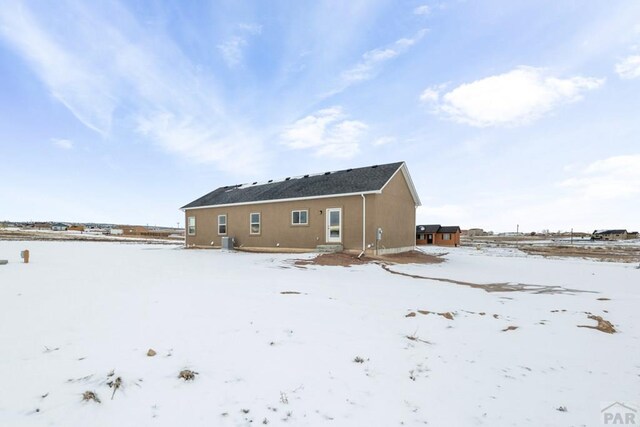 snow covered house featuring central AC and stucco siding