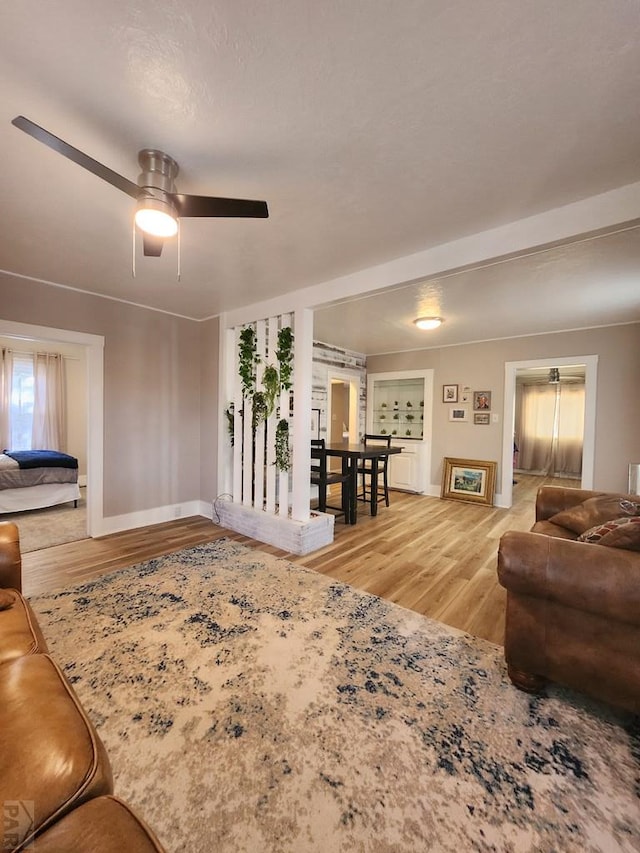 living area featuring a ceiling fan, light wood-style flooring, and baseboards