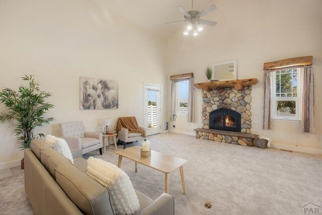 living room with light carpet, a stone fireplace, a high ceiling, and a wealth of natural light