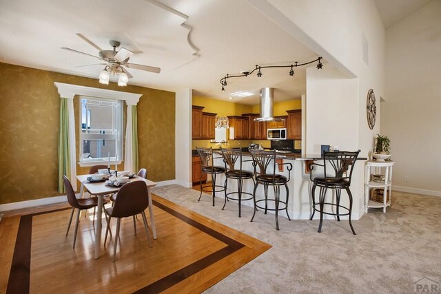 dining area featuring rail lighting, ceiling fan, baseboards, and light colored carpet