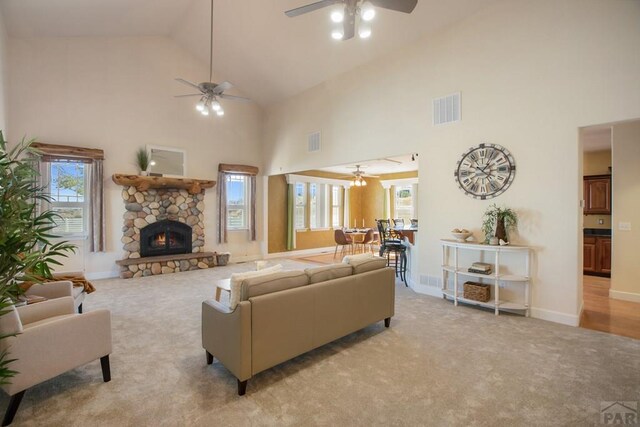 living area with light carpet, ceiling fan, visible vents, and a stone fireplace