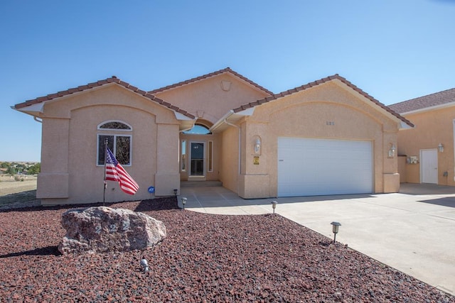 mediterranean / spanish home featuring an attached garage, a tiled roof, concrete driveway, and stucco siding