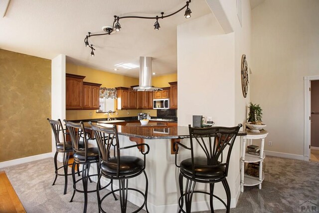 kitchen featuring a breakfast bar area, a peninsula, a sink, brown cabinets, and island exhaust hood