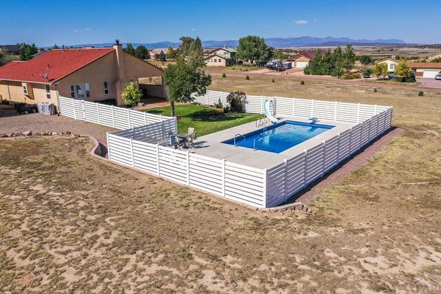 outdoor pool with a patio, a water slide, a fenced backyard, a mountain view, and a diving board