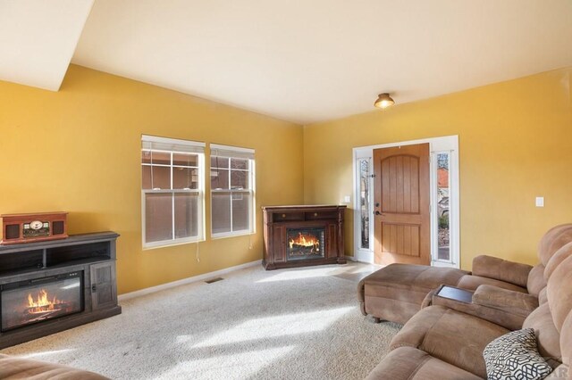 living room featuring carpet floors, visible vents, baseboards, and a glass covered fireplace