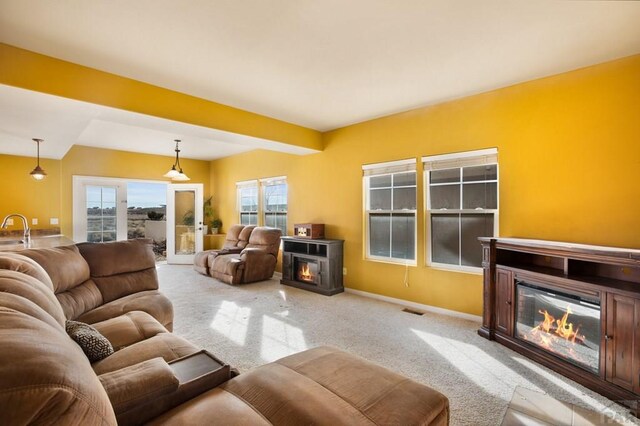 living area with a glass covered fireplace, visible vents, light carpet, and baseboards