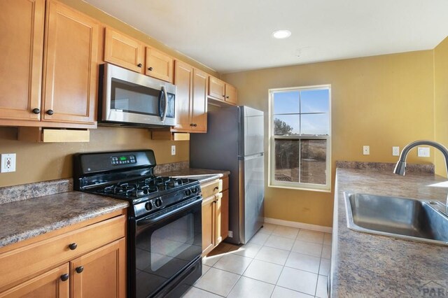 kitchen with light tile patterned floors, dark countertops, appliances with stainless steel finishes, a sink, and baseboards