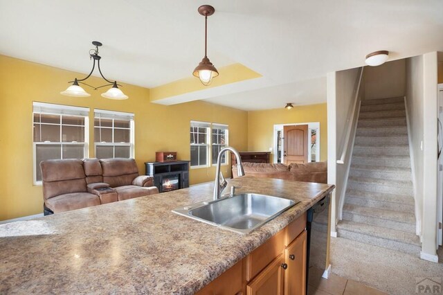 kitchen with light carpet, dishwasher, open floor plan, hanging light fixtures, and a sink