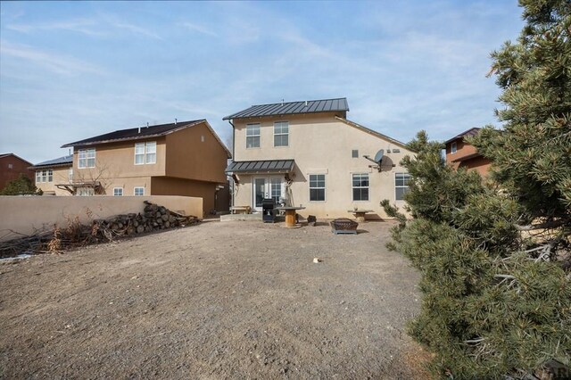 rear view of house with an outdoor fire pit, metal roof, a standing seam roof, fence, and stucco siding