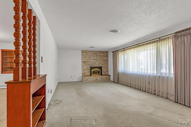 unfurnished living room with visible vents, light colored carpet, baseboard heating, a textured ceiling, and a fireplace