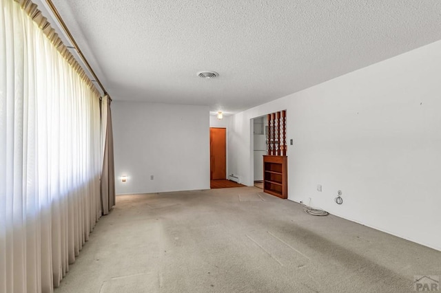 empty room with baseboard heating, visible vents, light carpet, and a textured ceiling