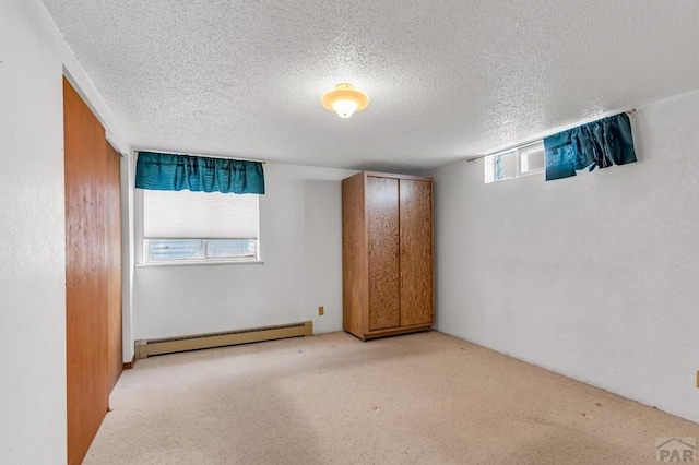 unfurnished room with light carpet, plenty of natural light, a baseboard heating unit, and a textured ceiling