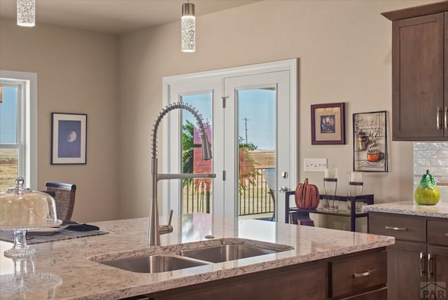 kitchen with hanging light fixtures, light stone countertops, dark brown cabinets, and a sink