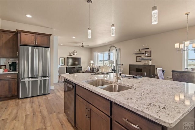 kitchen with stainless steel appliances, a sink, light wood-style floors, open floor plan, and hanging light fixtures