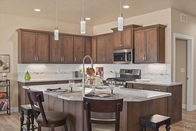 kitchen featuring stainless steel appliances, visible vents, hanging light fixtures, and light stone countertops