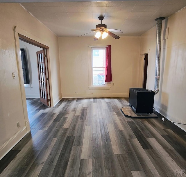 interior space with dark wood-style floors, ceiling fan, a wood stove, and baseboards