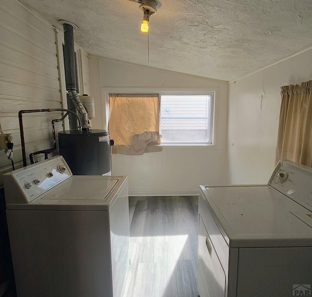 laundry area featuring washer and dryer, water heater, a textured ceiling, and wood finished floors