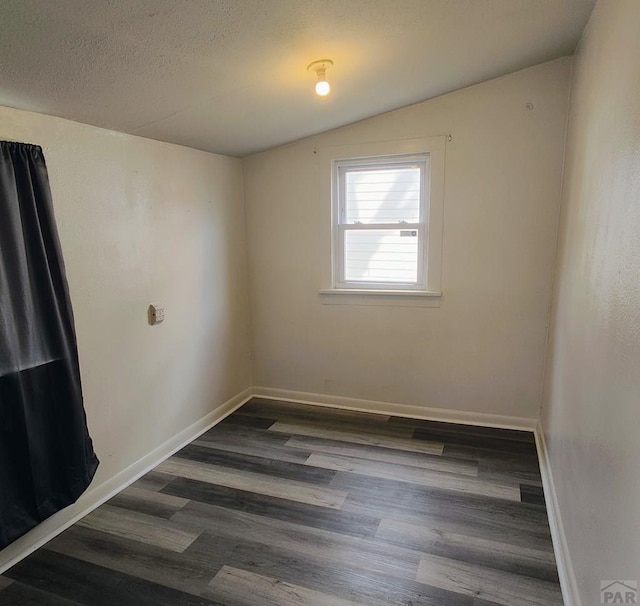 spare room featuring dark wood-style floors, a textured ceiling, lofted ceiling, and baseboards