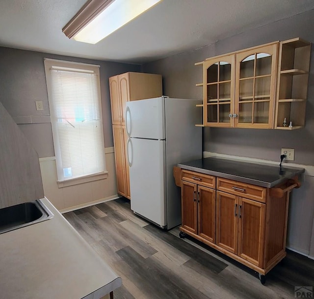 kitchen featuring dark wood-type flooring, freestanding refrigerator, open shelves, dark countertops, and glass insert cabinets