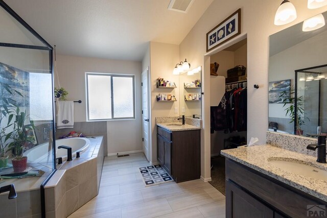 full bathroom with visible vents, two vanities, a sink, a spacious closet, and a bath