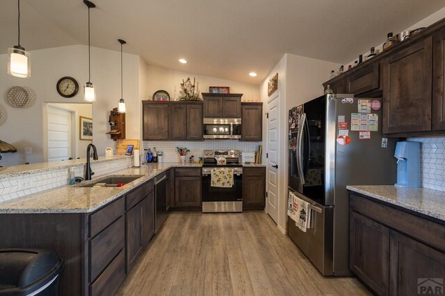 kitchen with stainless steel appliances, a peninsula, a sink, light stone countertops, and decorative light fixtures