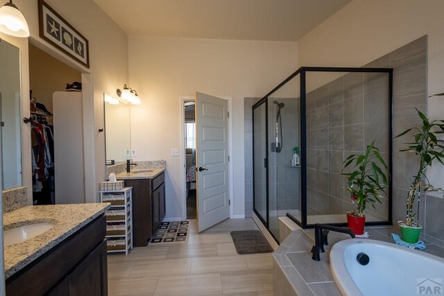 full bath with a sink, a stall shower, a walk in closet, and two vanities