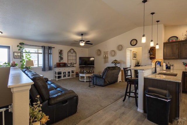 living area featuring a ceiling fan, light colored carpet, vaulted ceiling, and light wood-style flooring