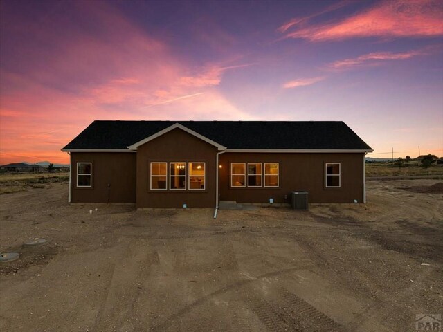 back of property at dusk with central AC and stucco siding