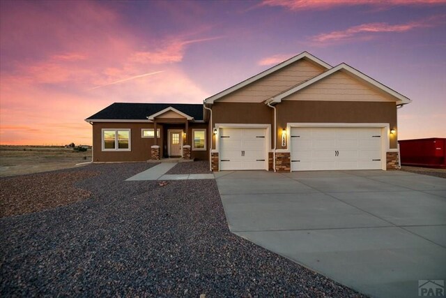 view of front facade featuring concrete driveway, stone siding, an attached garage, and stucco siding