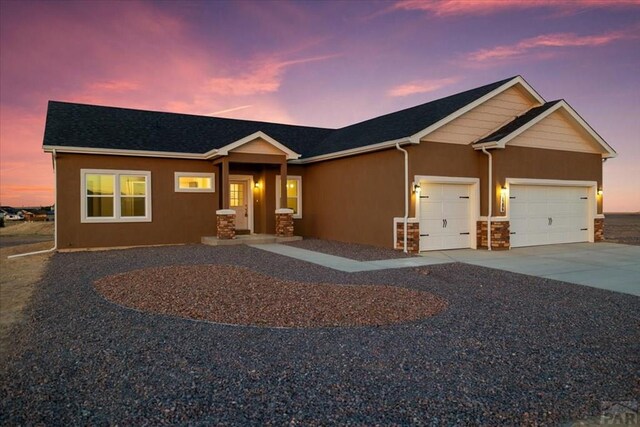 view of front of property featuring stone siding, driveway, an attached garage, and stucco siding