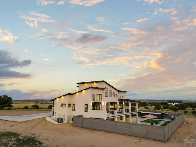 back of property at dusk with central air condition unit, stucco siding, a patio, and fence