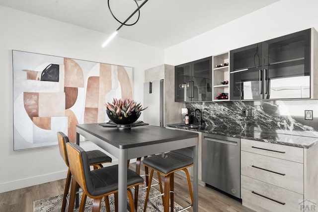 kitchen with modern cabinets, a sink, tasteful backsplash, stainless steel dishwasher, and light wood finished floors