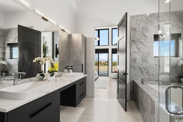 bathroom featuring double vanity, a high ceiling, tiled tub, and a sink