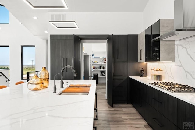 kitchen featuring a sink, appliances with stainless steel finishes, wall chimney range hood, modern cabinets, and dark cabinets