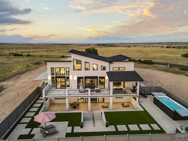 back of house at dusk with stucco siding, a swimming pool, a fenced backyard, a balcony, and a patio area