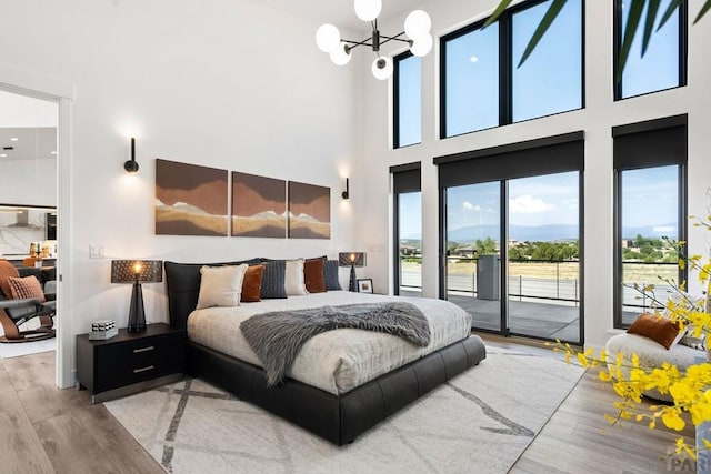 bedroom featuring access to exterior, a notable chandelier, a towering ceiling, and wood finished floors