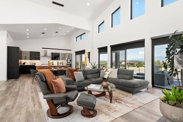 living room featuring recessed lighting, light wood-style floors, and a towering ceiling